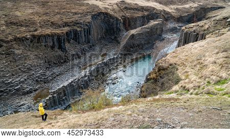 Woman Standing By The Studlagil Basalt Canyon, Iceland. This Is A Rare Volcanic Basalt Column Format