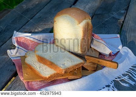 A Freshly Baked Loaf Of White Wheat Bread On A Wooden Table In The Garden. Thick Slices Of Bread Cut