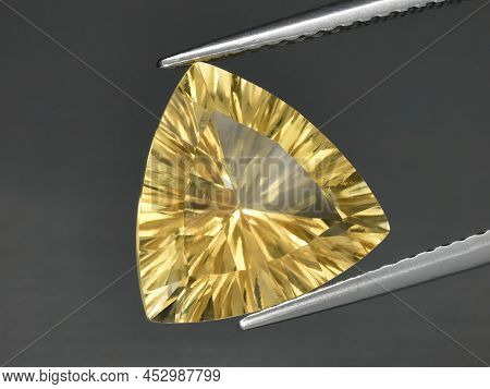 Natural Gemstone Yellow Citrine In Tongs On A Gray Background