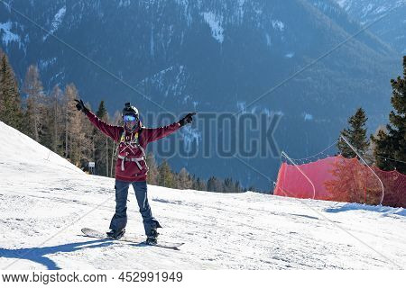 Snowboarder With Arms Outstretched Standing On Snowy Mountain Slope On Sunny Day