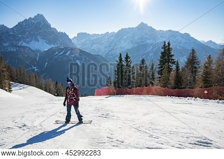 Snowboarder Standing On Snowy Mountain Slope At Winter Resort On Sunny Day