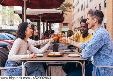 Multiethnic Group Of 4 Friends Toasting On A Restaurant Terrace