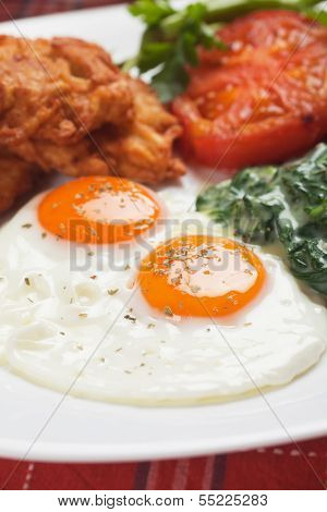 Fried eggs served for breakfast with spinach, fried tomato and potato pancakes