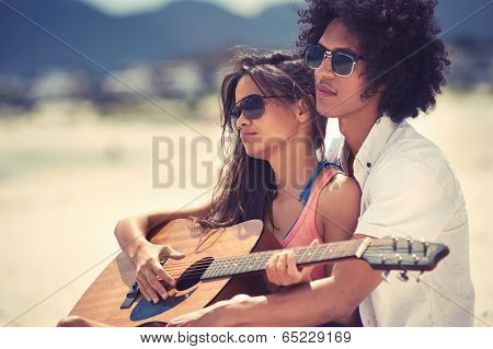 Cute hispanic couple playing guitar serenading on beach in love and embrace