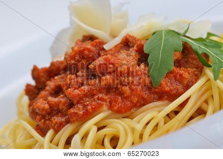 Italian spaghetti topped with bolognaise, or bolognese, sauce with tomatoes, meat and cheese on a plain white plate