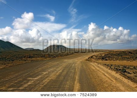 dasty road in desert under cloudy sky