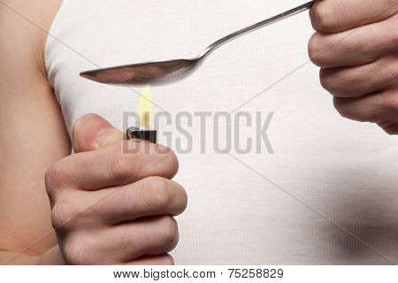 Man with a hardline drug addiction heating drugs in a spoon over a flame 