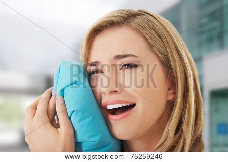 Woman having tooth ache holding ice bag near face
