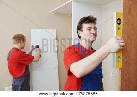 Two carpenters workers joint and settle home built-in cupboard