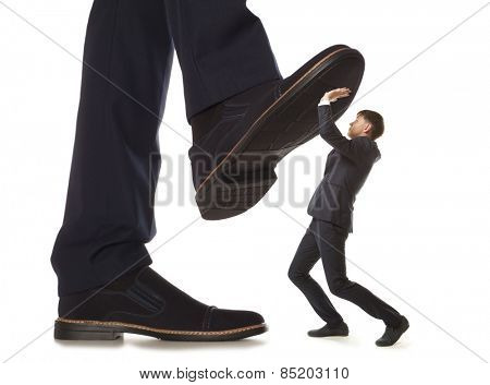 Cared small businessman under big leg his boss, isolated on white background