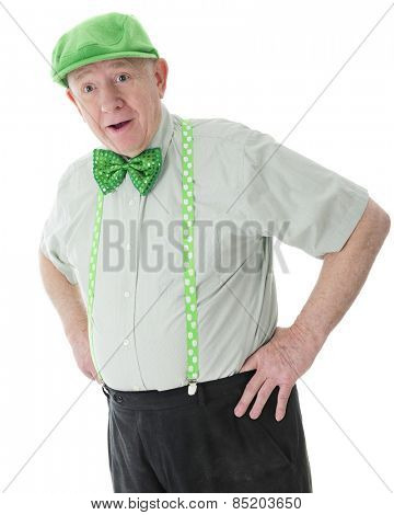 A surprised senior adult man looking happily surprised in his green hat, tie and shamrock-adorned suspenders.  On a white background.