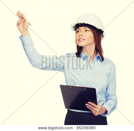 building, developing, consrtuction and architecture concept - smiling businesswoman in white helmet with clipboard pointing finger