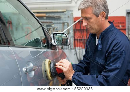 Portrait Of Mature Auto Mechanic Polishing Car At Workshop