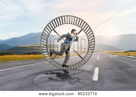 Young businessman running in huge hamster wheel