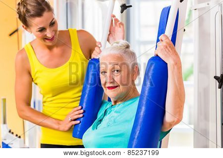 Senior woman with trainer exercising chest using butterfly machine in fitness gym