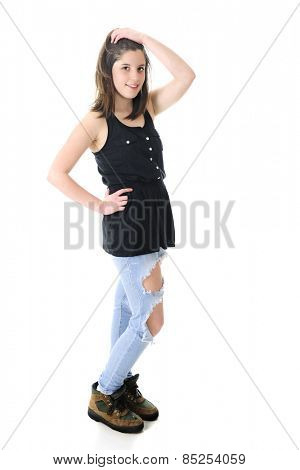 Full length image of a pretty teen brunette standing in her sleeveless black top, holey denim jeans and work boots.  On a white background.