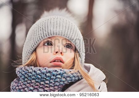 close up outdoor winter portrait of cute dreamy toddler girl in grey hat and scarf