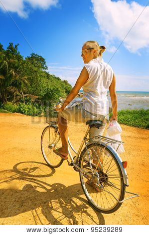 Young Woman Riding Bicycle Across River Bridge Next To Tropical Park