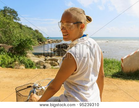Young Woman Riding Bicycle Across River Bridge Next To Tropical Park