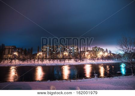 the little river and the multi-storey houses at the distant shore at snowy night