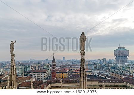 View over Milan from the top of the gothic cathedral Duomo di Milano (Milan Cathedral) Italy. Church's roof statues in the foreground skyscrapers of the city in the background.
