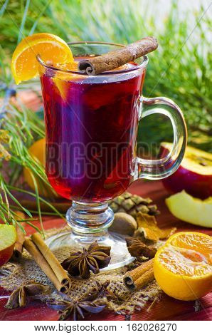 Spicy Christmas drink in a glass with spices on a background of trees