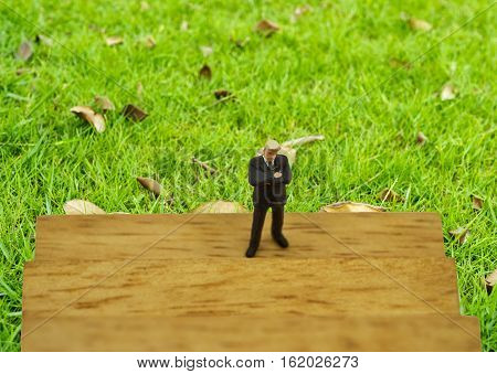 abstract mini businessman stand on wood block with green feilds background - can use to display or montage on product