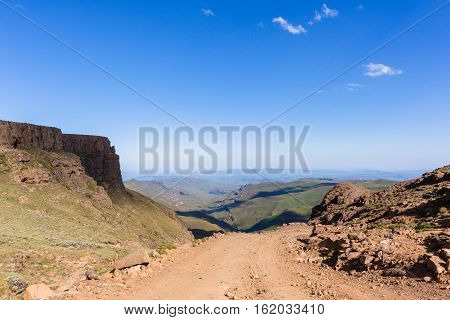 Mountains valley rugged dirt road steep pass overlooking horizon blue landscape.