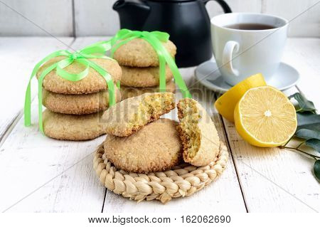 Shortbread lemon flavored cookies: a broken and connected green ribbon for a gift. Teapot and fresh lemon on a white wooden background. Close up