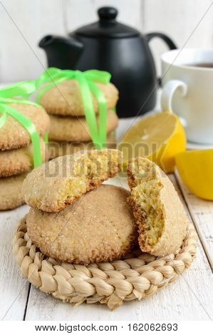 Shortbread lemon flavored cookies: a broken and connected green ribbon for a gift. Teapot and fresh lemon on a white wooden background. Close up