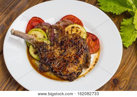 Pork steak on the bone grilled with vegetables. Wooden background