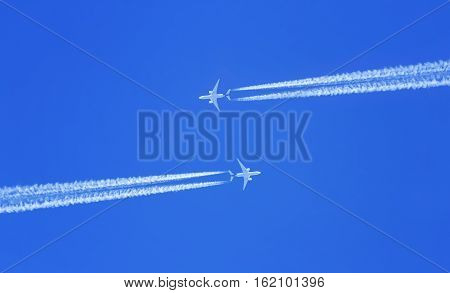 two planes flying high in the sky meet, leaving white streaks