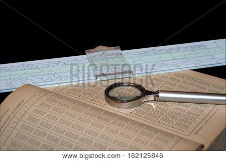 Handbook of mathematics magnifying glass and a slide rule isolated on black background