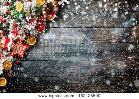 Merry Christmas Frame with Snow and wood green pine, colorful baubles, knots with berries,stars, orangesand other seasonal stuff over an old wooden aged background