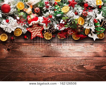 Merry Christmas Frame with green pine, colorful baubles, knots with berries,stars, orangesand other seasonal stuff over an old wooden aged background
