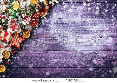 Merry Christmas Frame with Snow and wood green pine, colorful baubles, knots with berries,stars, orangesand other seasonal stuff over an old wooden aged background