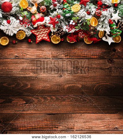 Merry Christmas Frame with green pine, colorful baubles, knots with berries,stars, orangesand other seasonal stuff over an old wooden aged background