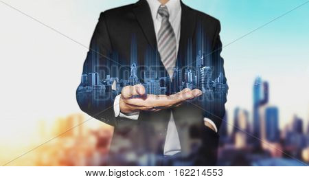 Double exposure businessman holding blue city hologram, with city in sunrise background, real estate business technology concepts
