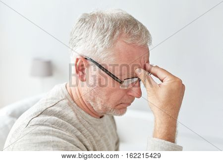 healthcare, pain, stress, age and people concept - senior man suffering from headache at home