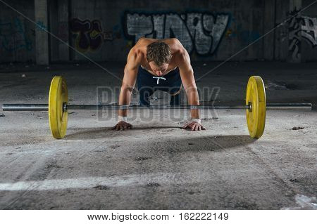 Front view of man doing push-ups near barbell. Horizontal indoor shot