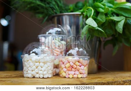 Desserts choice. Marshmallow chewing candies for hot chocolate topping in glass jars on counter bar for sale. Traditional american sweets for sale, closeup