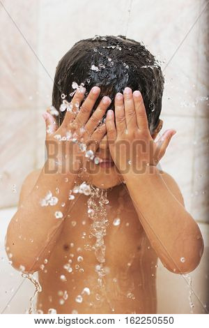 Happy baby in the bath hands on his face water splash
