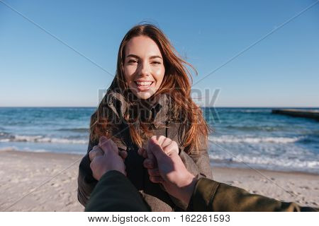 First person view of man holding hands of happy woman on the beach.