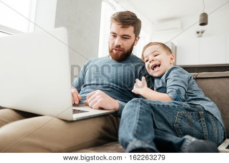 Picture of cheerful father using laptop computer with his little cute son.