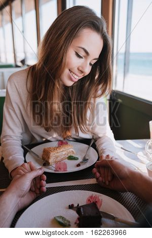 Vertical image of shy woman sitting by the table with food on date in cafe near the sea. First-person view