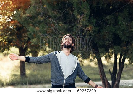 Smiling man enjoying wind blowing in forest. Happy man feeling joy while walking at nature, free space on green trees background. Life love, joy, fresh air, renovation concept