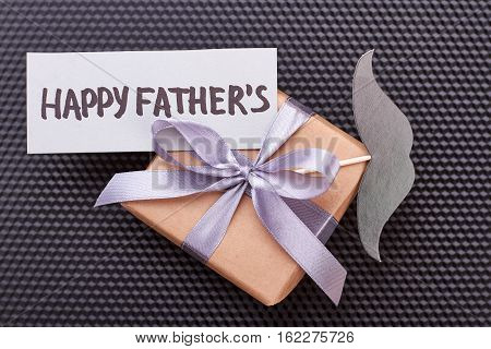 Father's Day card on gift. Mustache, present box, black backdrop. Father will be happy.