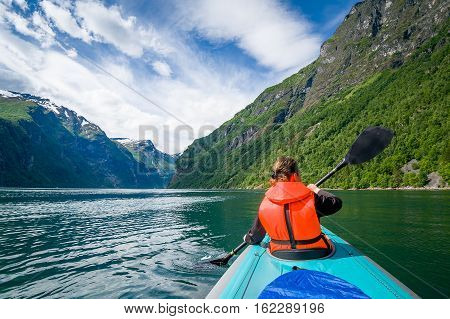 Woman kayaker in bright orange life vest on her trip in Geiranger fjord waters. Geirngerfjord, Norway.