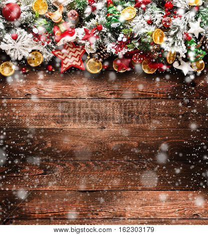 Merry Christmas Frame with Snow and wood green pine, colorful baubles, knots with berries,stars, orangesand other seasonal stuff over an old wooden aged background