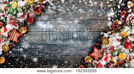Merry Christmas Frame with Snow and wood green pine, colorful baubles, knots with berries,stars, orangesand other seasonal stuff over an old wooden aged background